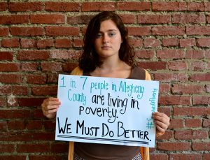 Just Harvest Bonner Leader holding sign: 1 in 7 people in Allegheny County are living in poverty. We Must Do Better.