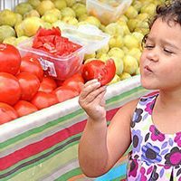girl tasting tomato at farmers market