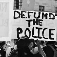 Protester with Defund the Police sign via flickr/Taymaz Valley