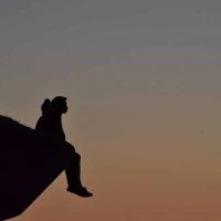 silhouette of person sitting on cliff