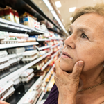 senior woman in dairy aisle of grocery store considering items in dairy case